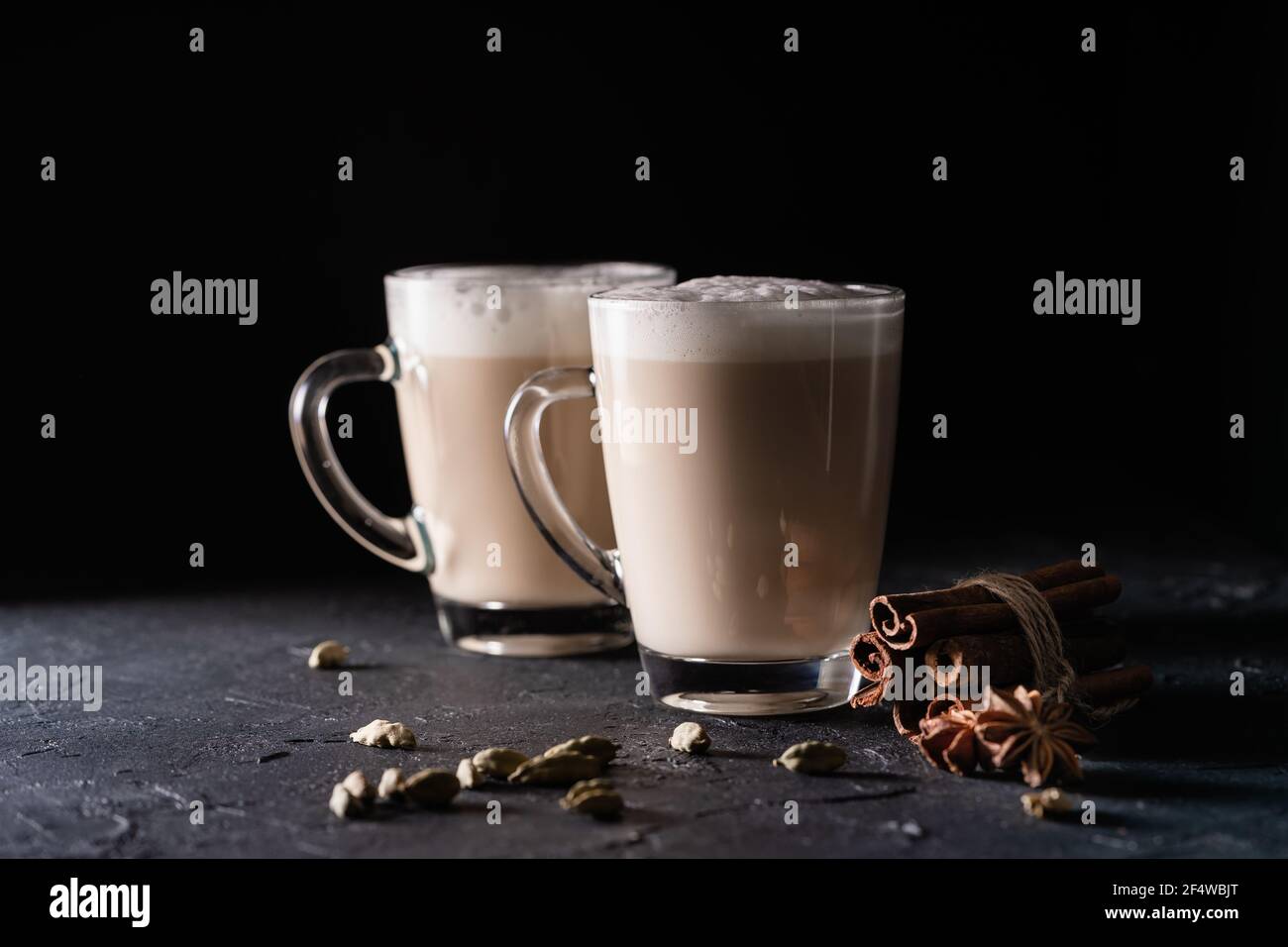 Two cups of Chai tea latte, hot tea drink with foamed milk on dark black background Stock Photo