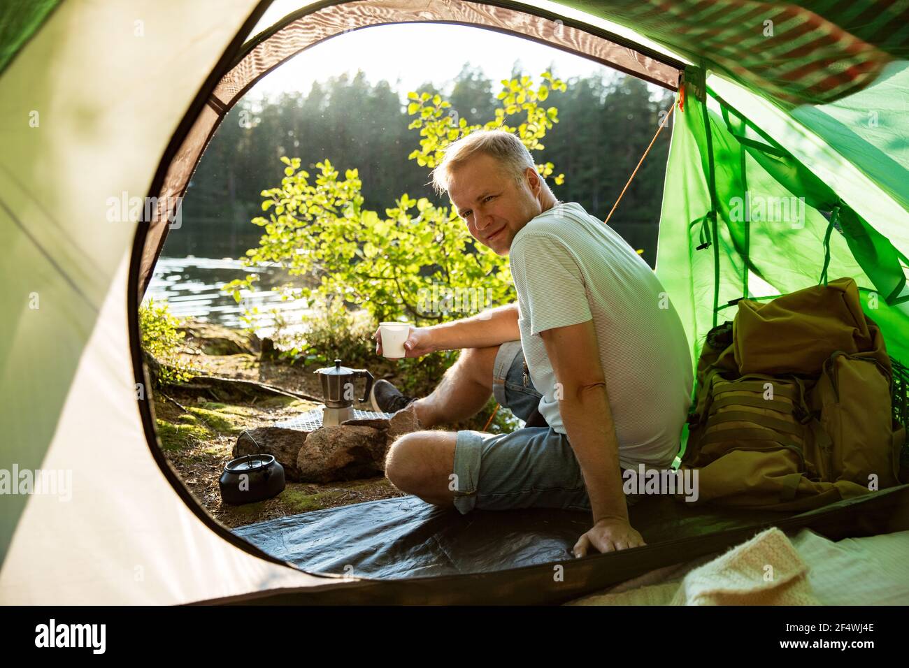 Man making coffee using espresso maker on campfire in forest on shore