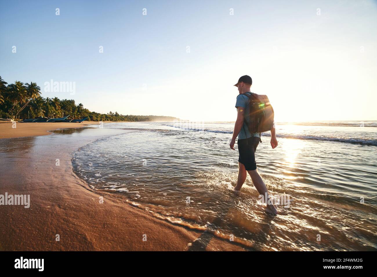 Solo traveler walking on empty beach. Rear view of man with backpack at sunrise. Beautiful sandy coast near Tangalle in Sri lanka. Stock Photo