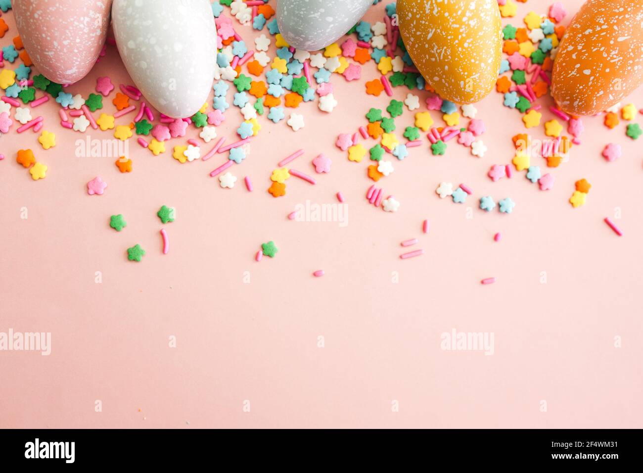 White, grey and yellow eggs on pink background with colourful sprinkles. Easter holiday background. Stock Photo