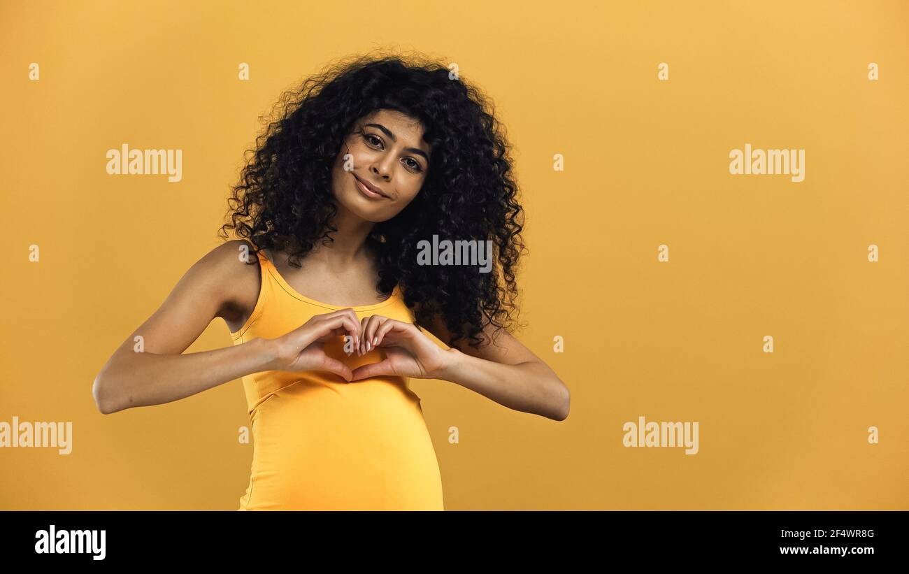Pregnant hispanic woman showing love sign isolated on yellow Stock Photo