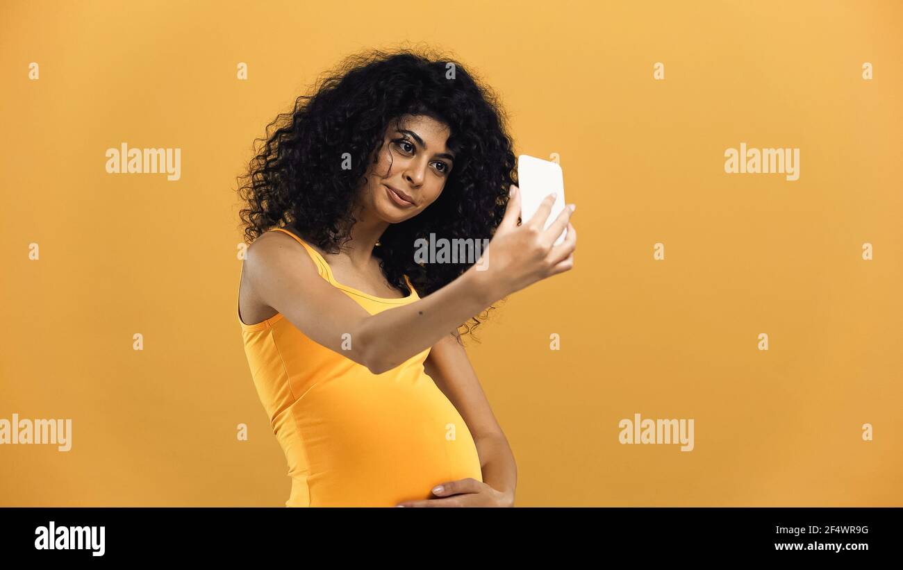 Pregnant hispanic woman taking selfie isolated on yellow Stock Photo