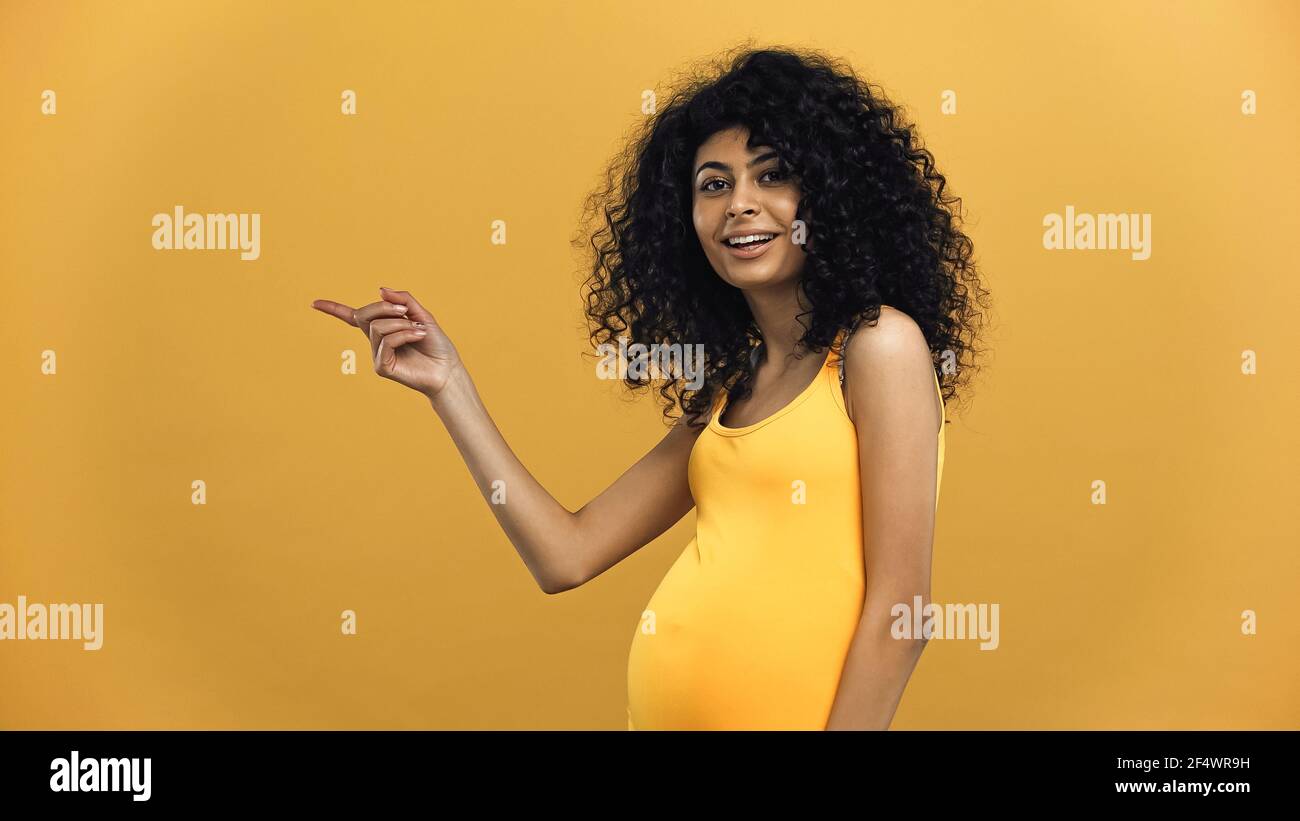 Pregnant hispanic woman pointing with finger isolated on yellow Stock Photo