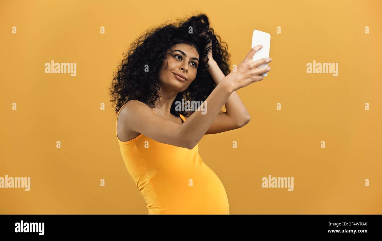 Pregnant hispanic woman taking selfie with smartphone isolated on yellow Stock Photo