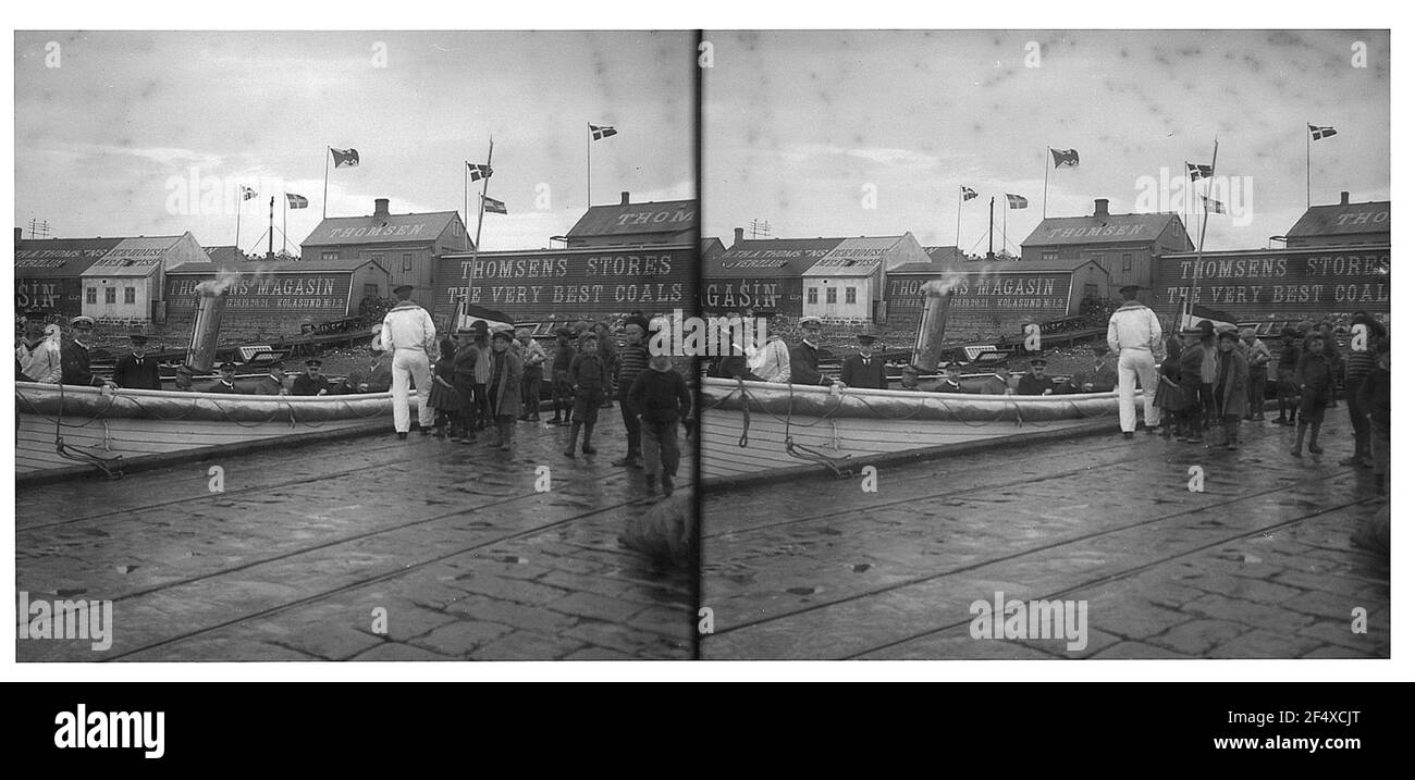 Tromsø? / Norway: Dock in the harbor. Houses with advertising for Thomsens carbon handles, flags of Hapag and Norway labor over the roofs; Tourists in boats when placing in the harbor, on the quay children and watch Stock Photo