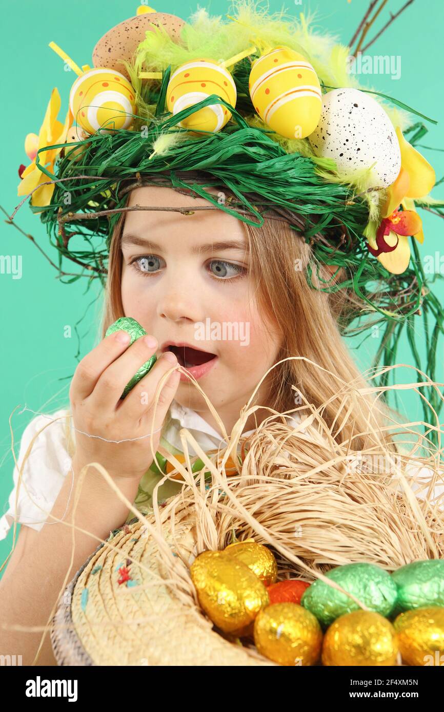 Cute little child wearing a fun hairstyle on Easter Day. Girl with basket of shiny eggs looks at an easter egg squinting Stock Photo