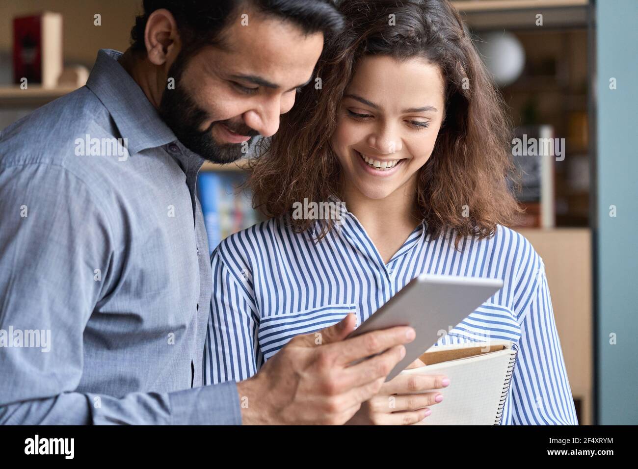 Smiling indian and latin colleagues talking using digital tablet in office. Stock Photo
