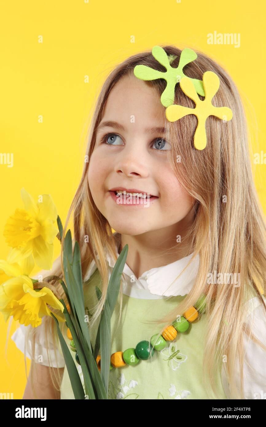 spring season concept: cute little girl with daffodil flowers for spring festival on yellow background. The child looks up to the side - Stock Image