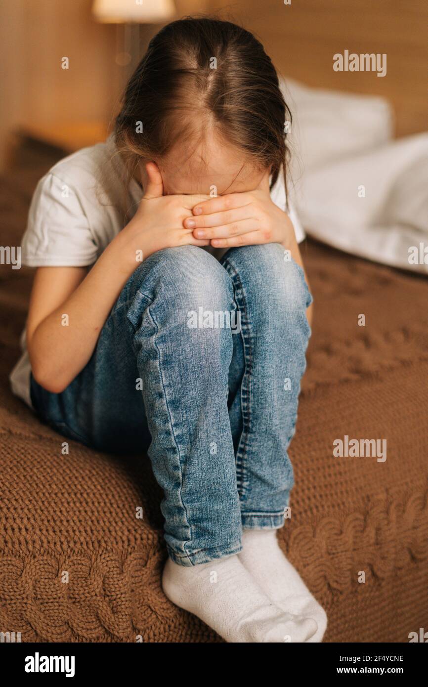 Closeup of disappointed little girl hugging knee, sobbing with head bowed and crying sitting