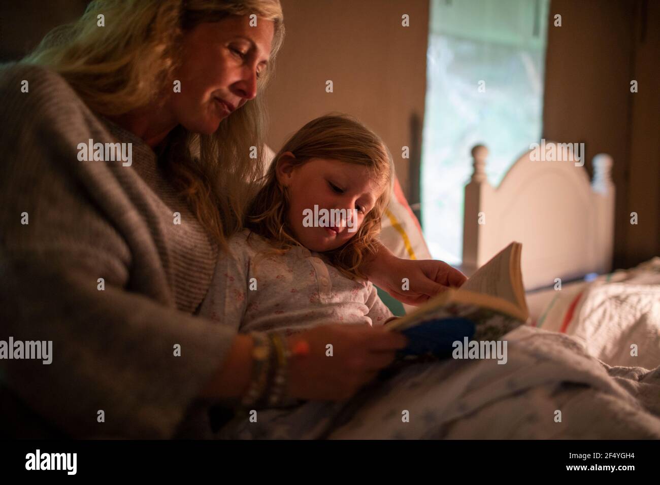 Mother reading bedtime story to daughter in bed Stock Photo
