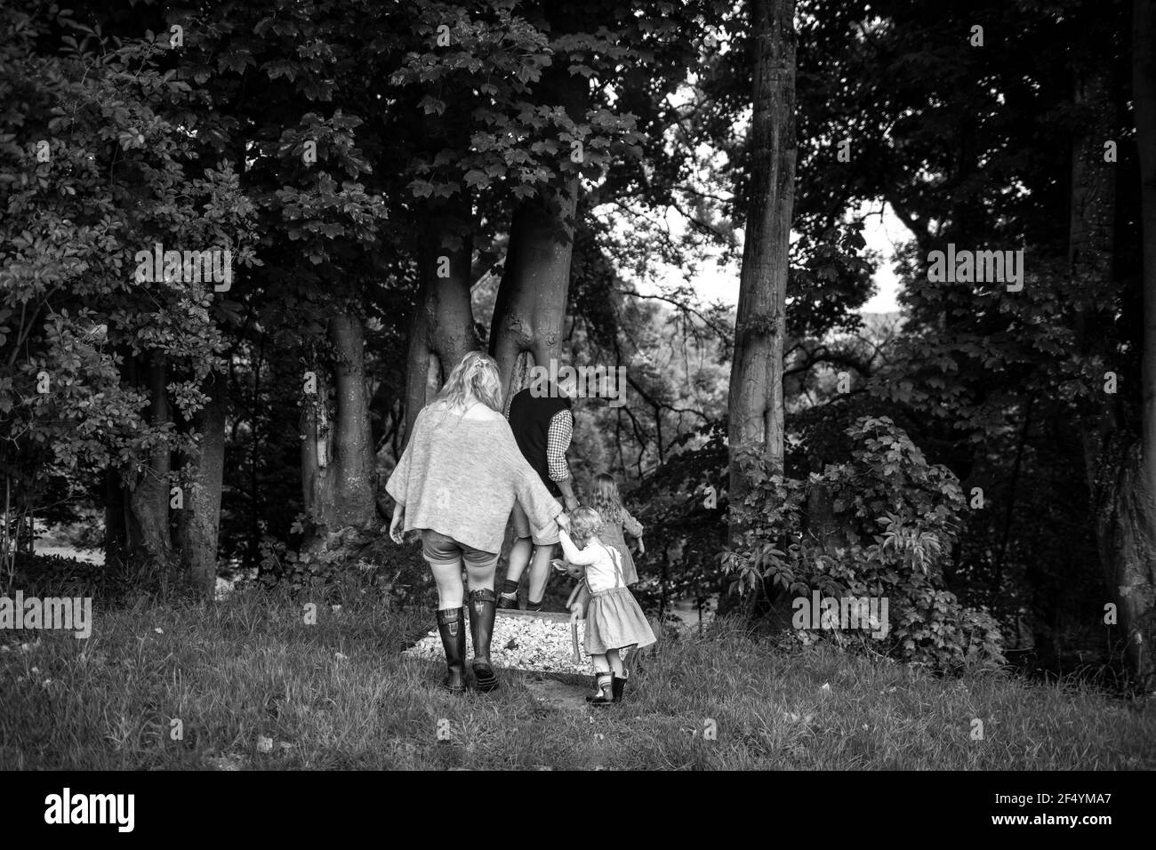Parents holding hands with daughters walking on path through trees Stock Photo