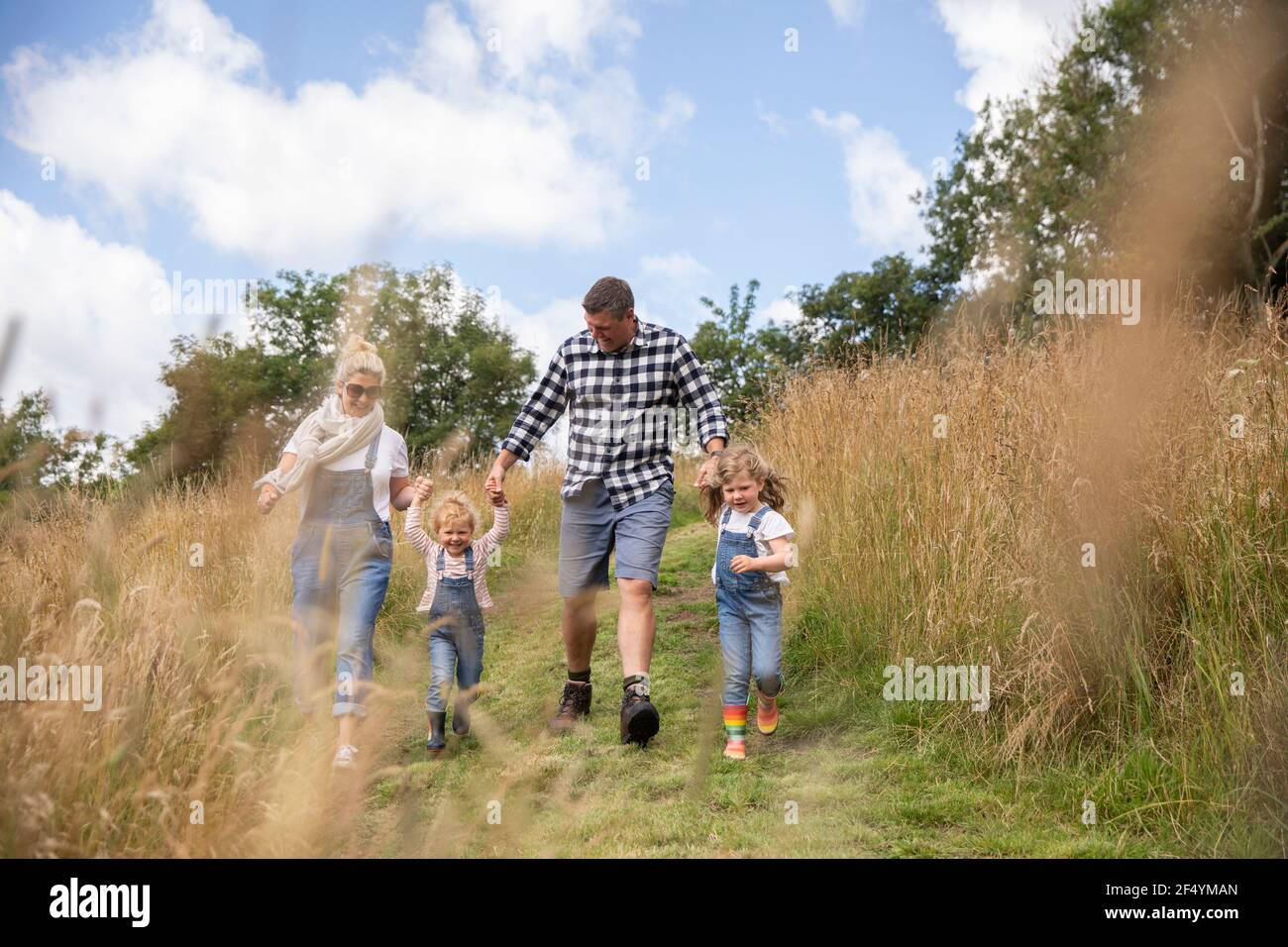 Happy family holding hands running in sunny rural field Stock Photo