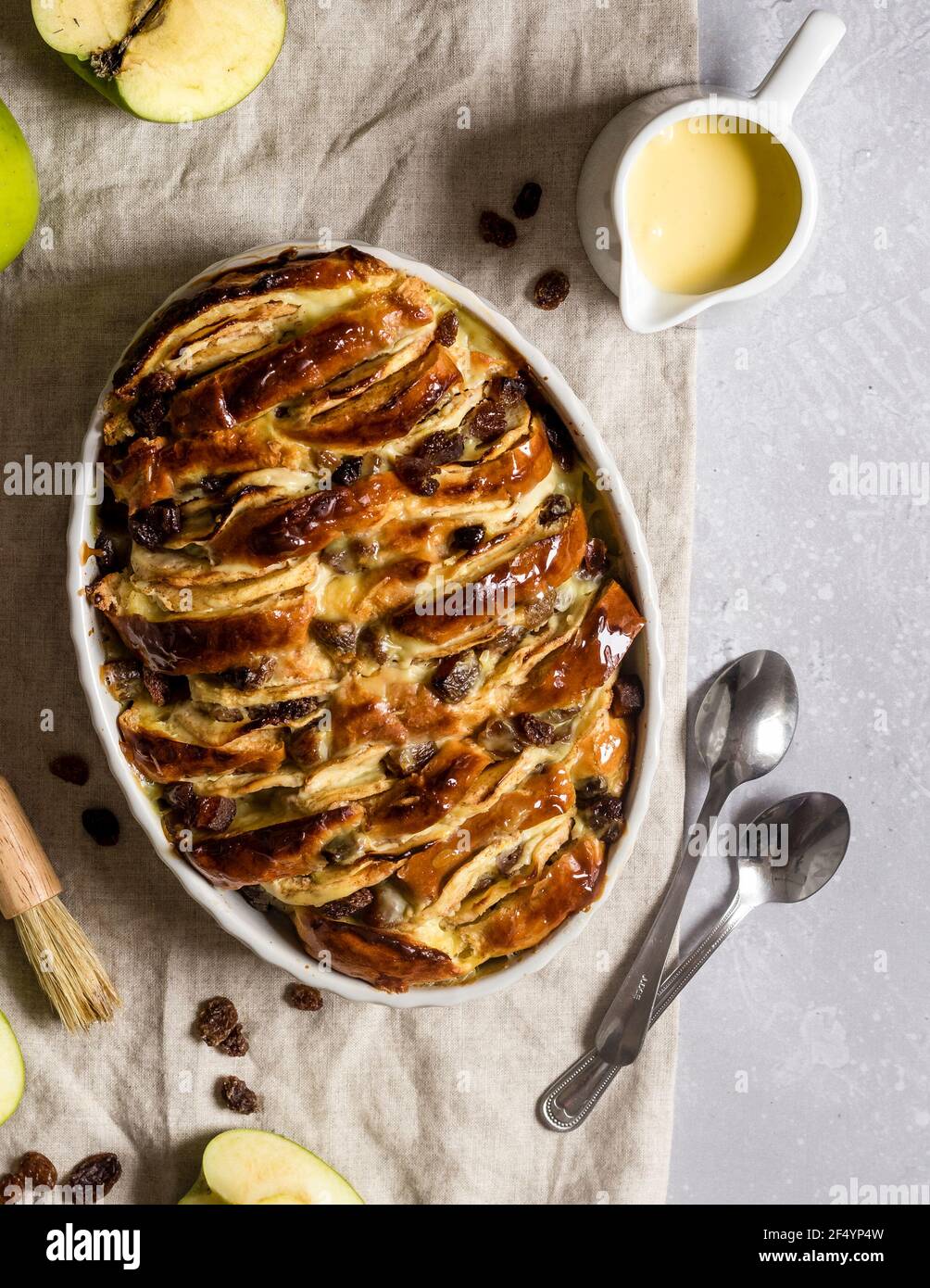 Afternoon scene with freshly prepared vegan brioche and apple pudding with raisins, dried apricots and custard lying on a table, ready to be served. Stock Photo