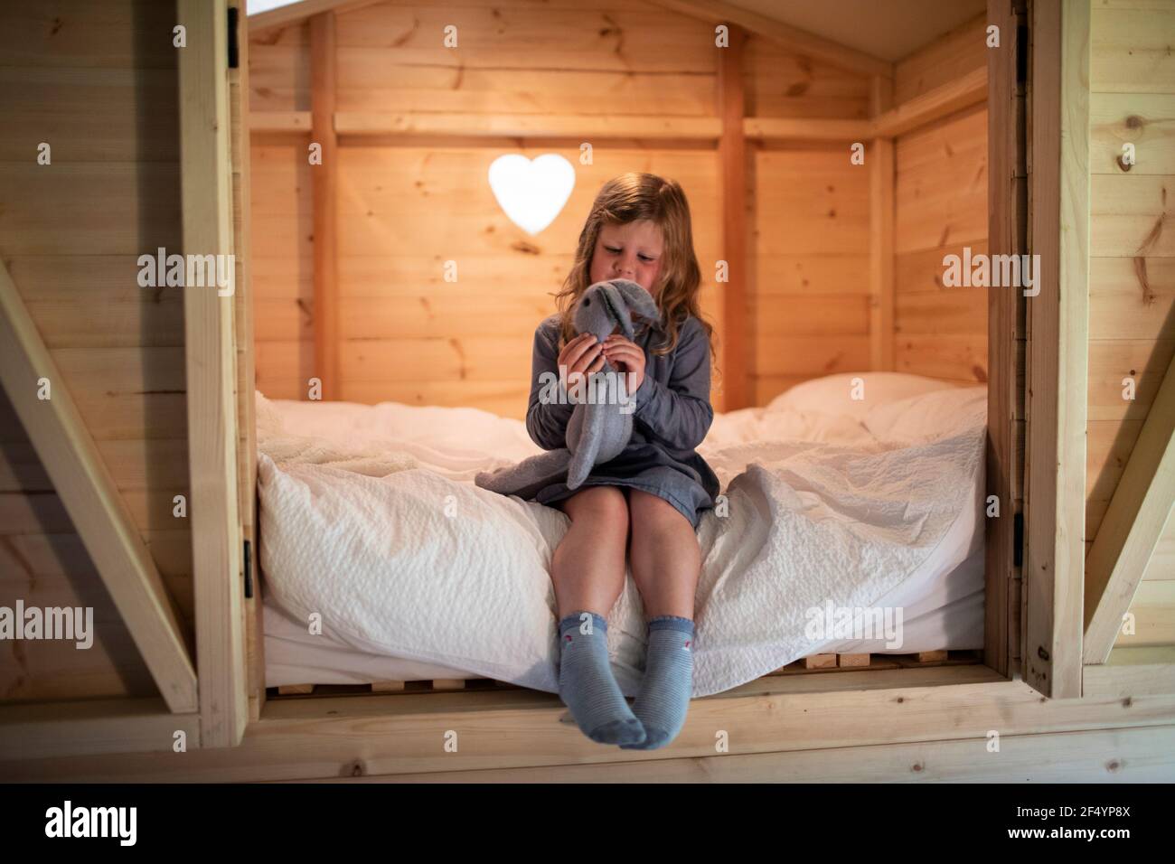 Cute girl playing with stuffed bunny on bed in wood loft Stock Photo