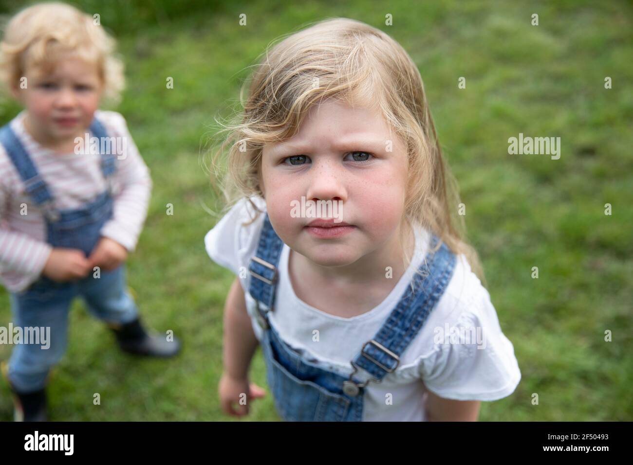 Portrait serious blonde girl in overalls with sister Stock Photo