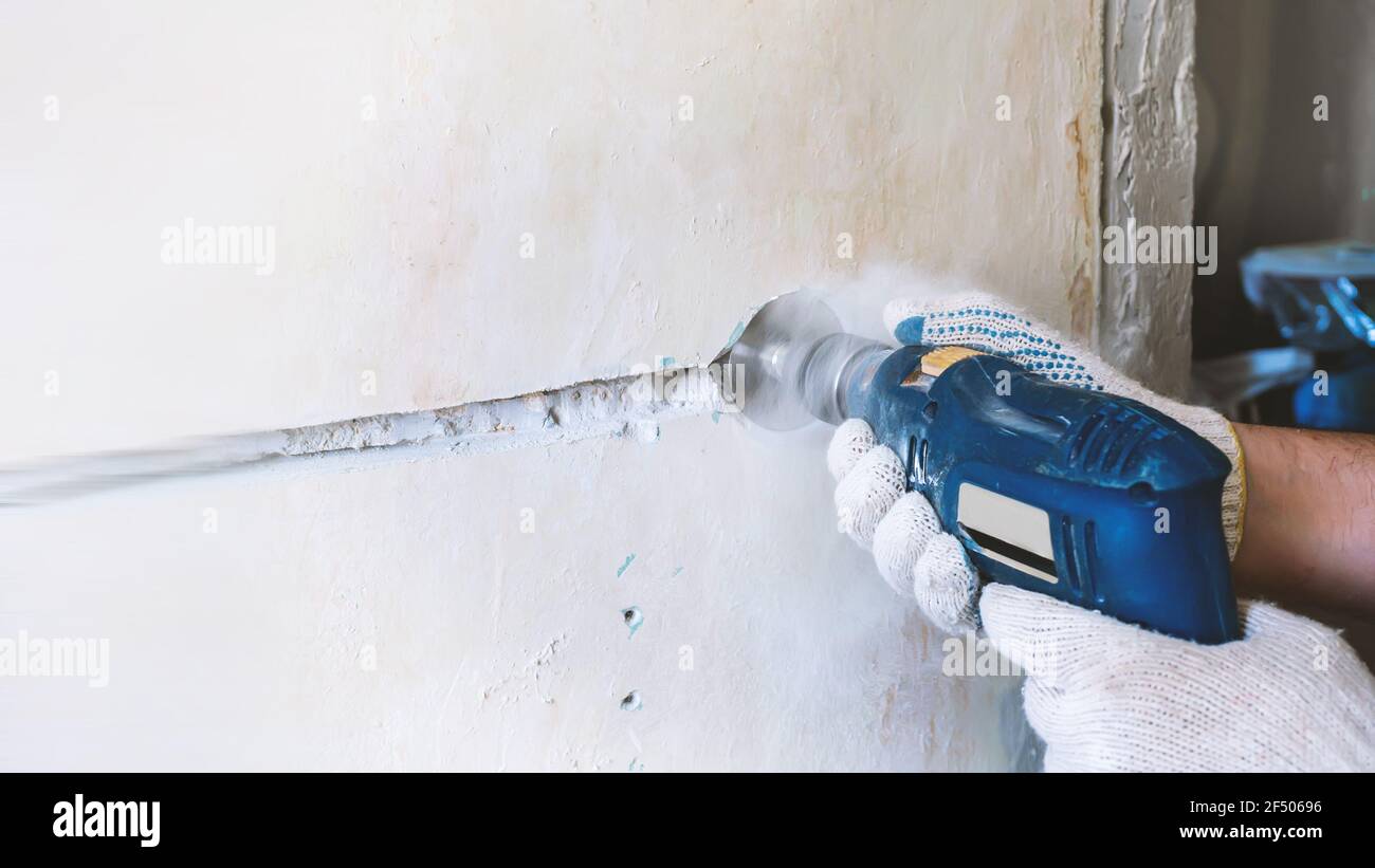 worker drills a hole for an electrical outlet in a concrete brick wall