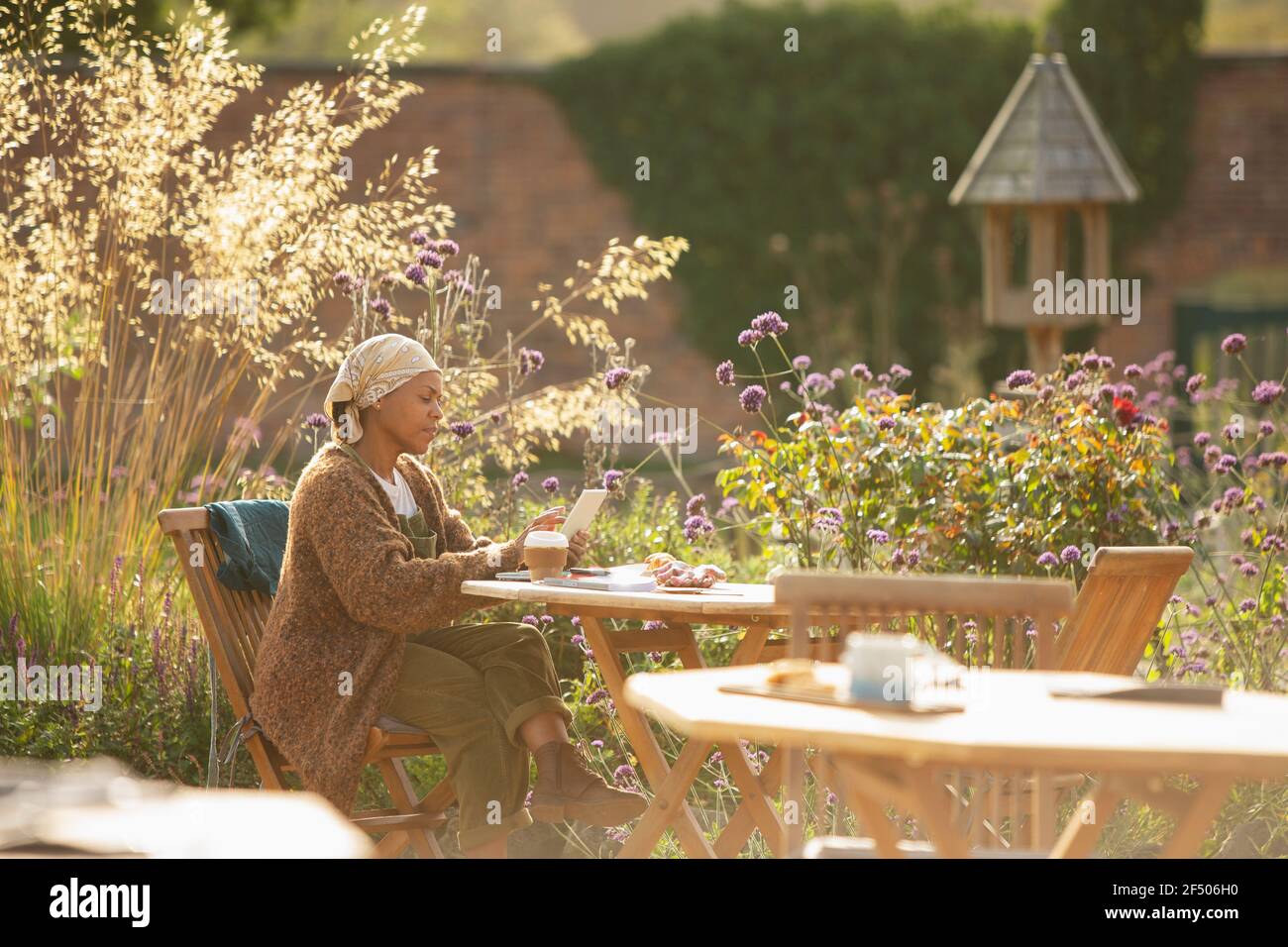 Woman with digital tablet and coffee at sunny garden cafe table Stock Photo