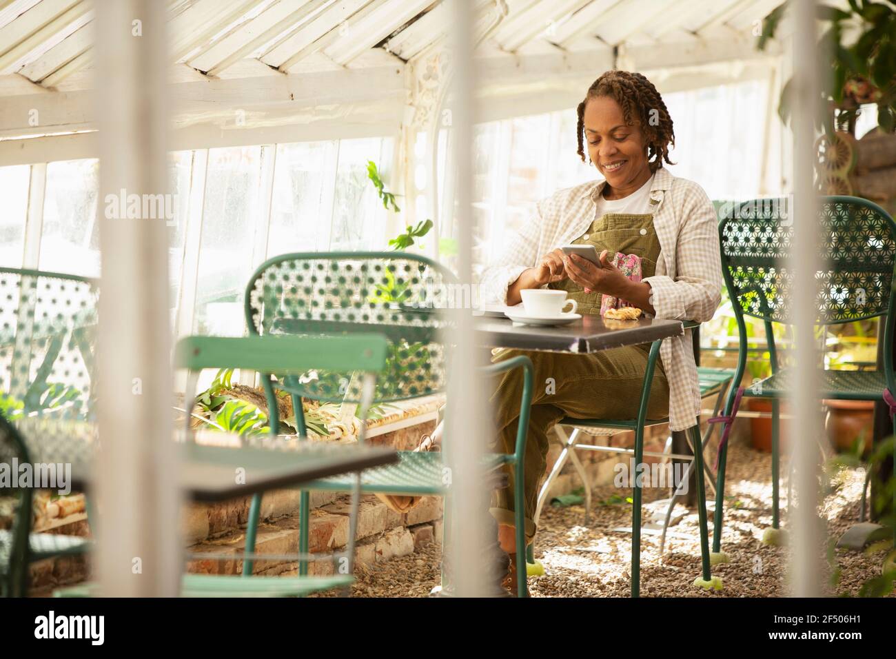 Woman with smart phone drinking tea in garden center greenhouse Stock Photo