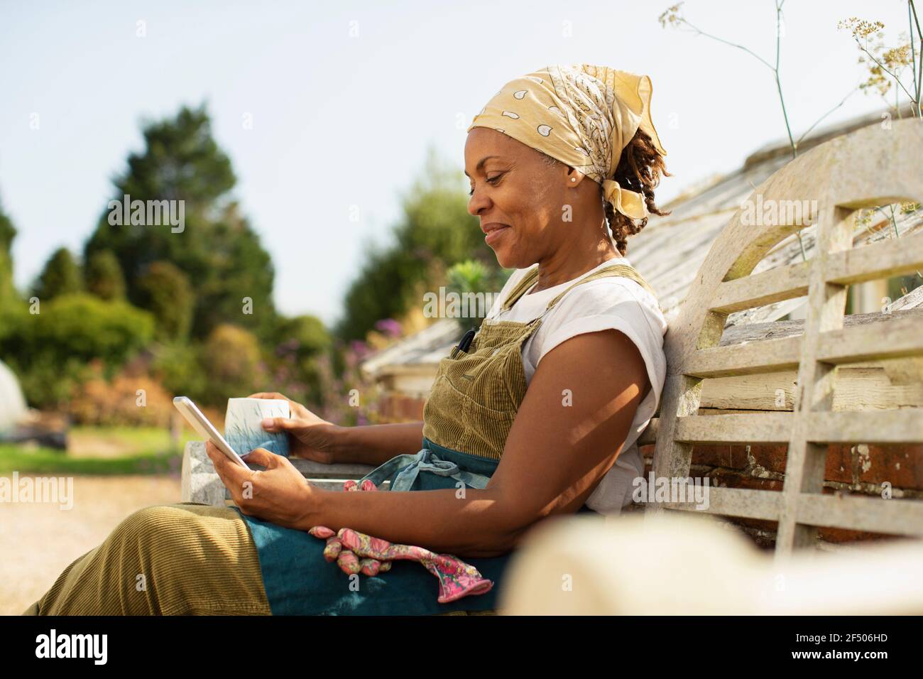 Female garden shop owner with smart phone and coffee on sunny bench Stock Photo