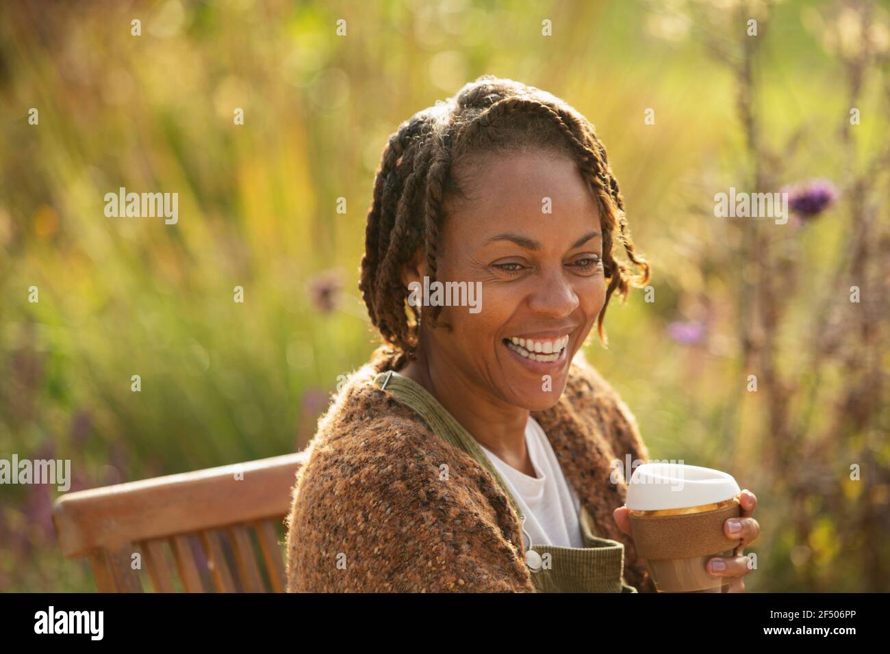 Happy woman with coffee laughing on sunny garden patio Stock Photo