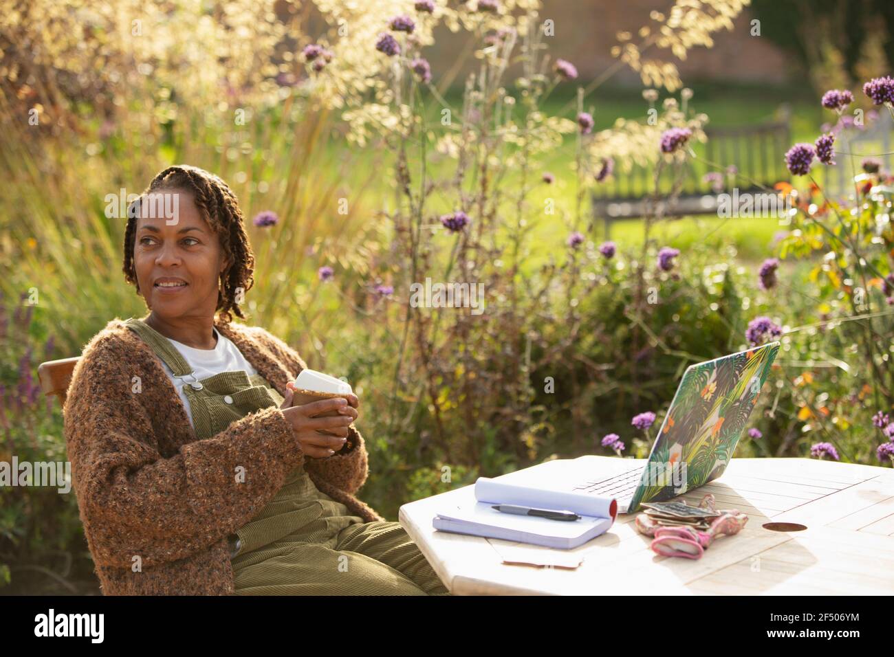 Woman with coffee working at laptop on idyllic garden patio Stock Photo