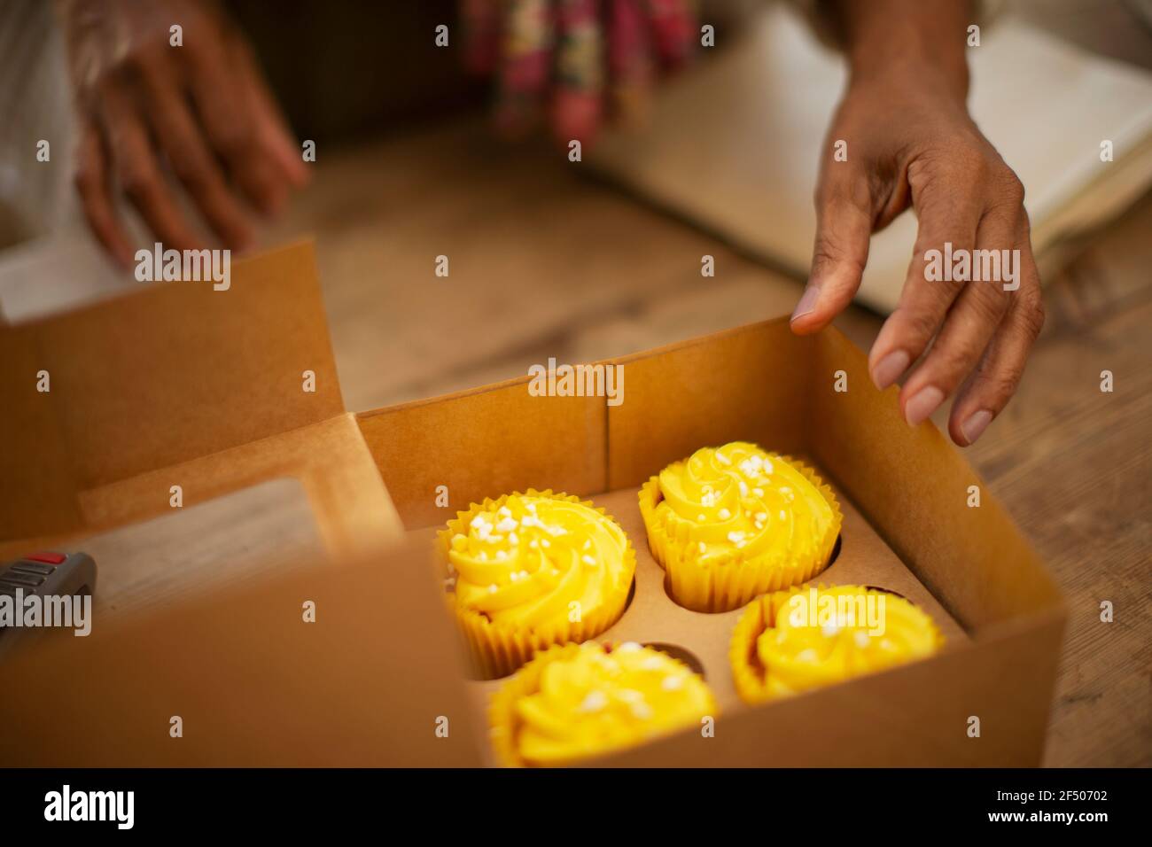 Woman reaching for lemon yellow cupcakes in bakery box Stock Photo