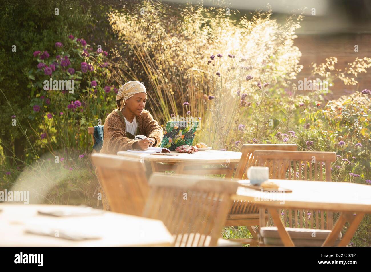 Woman working at laptop on sunny garden cafe patio Stock Photo