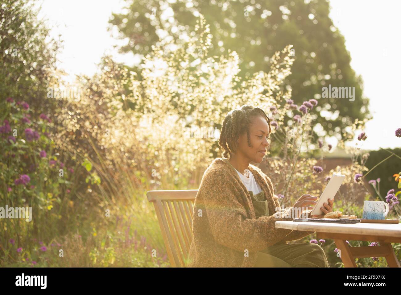 Woman using digital tablet at sunny idyllic garden patio table Stock Photo