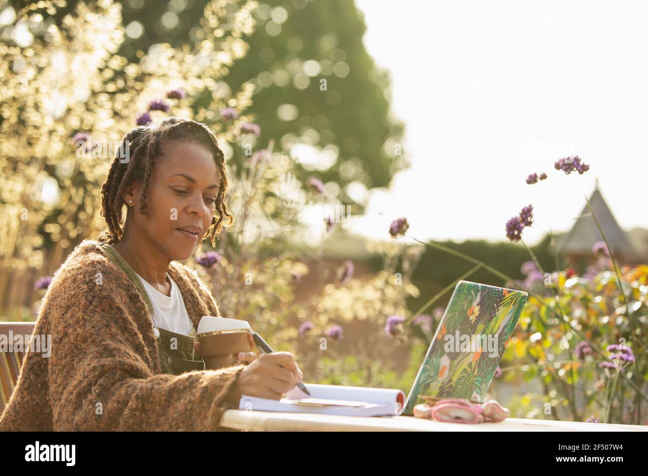 Woman with coffee working at laptop on sunny garden patio Stock Photo