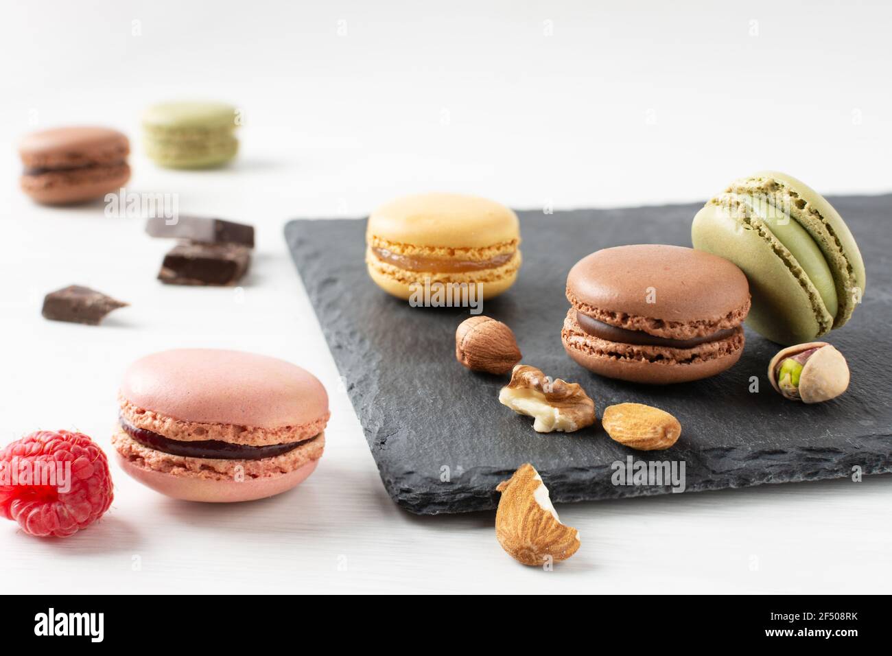 Variety of french macaroons with raspberry, nuts and chocolate on white wooden table. French meringue cookie macarons. Stock Photo