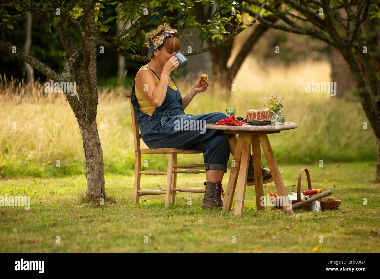 Woman taking break from gardening eating cake at garden table Stock Photo