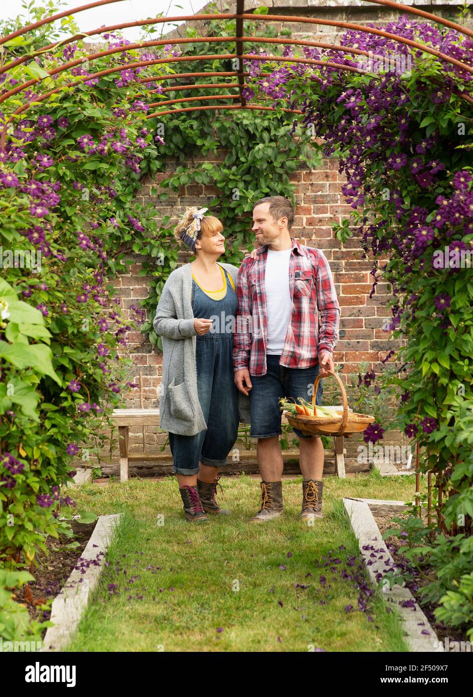 Couple harvesting vegetables below trellis with purple flowers Stock Photo