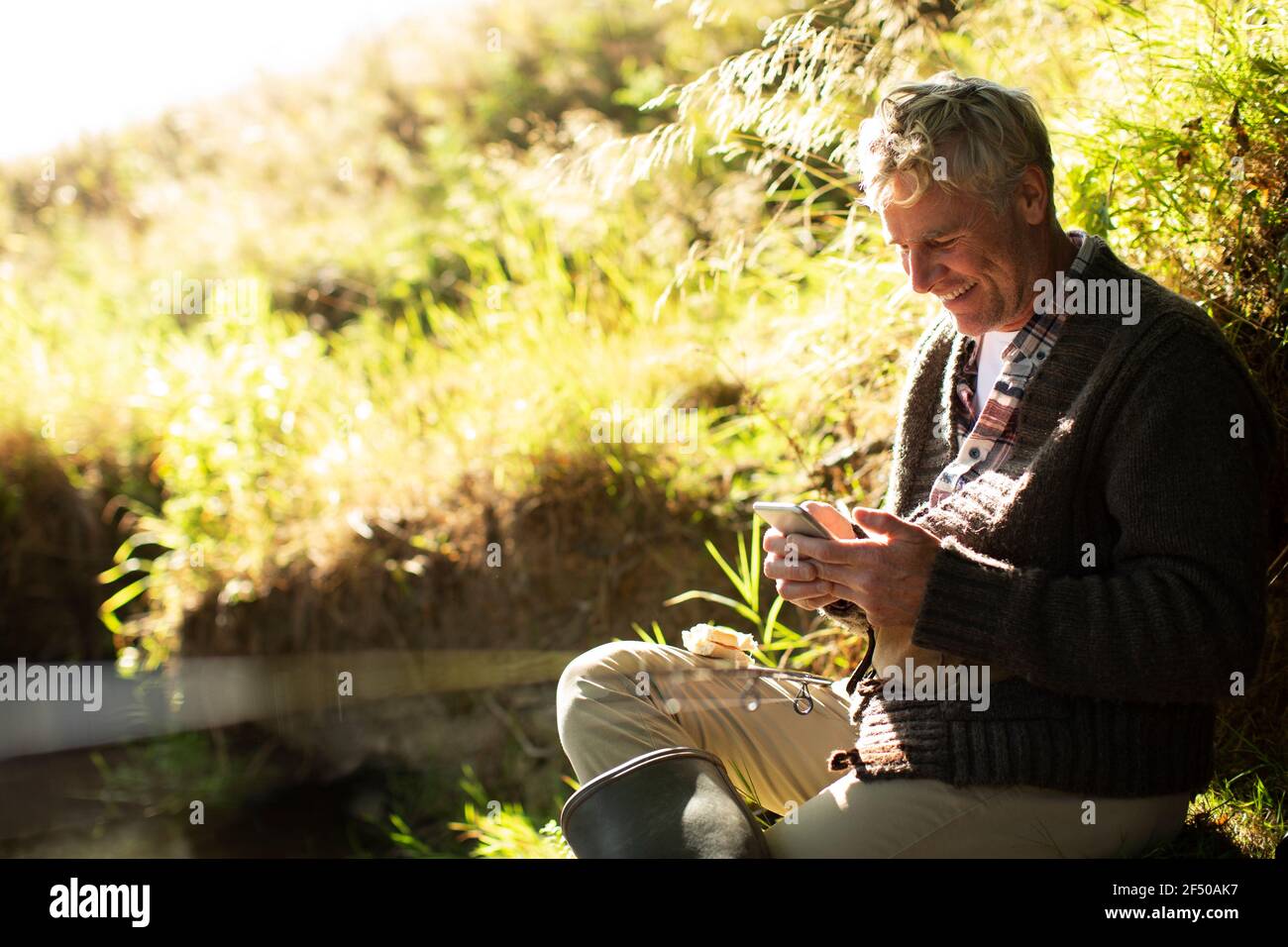 Man fly fishing and using smart phone on sunny riverbank Stock Photo ...
