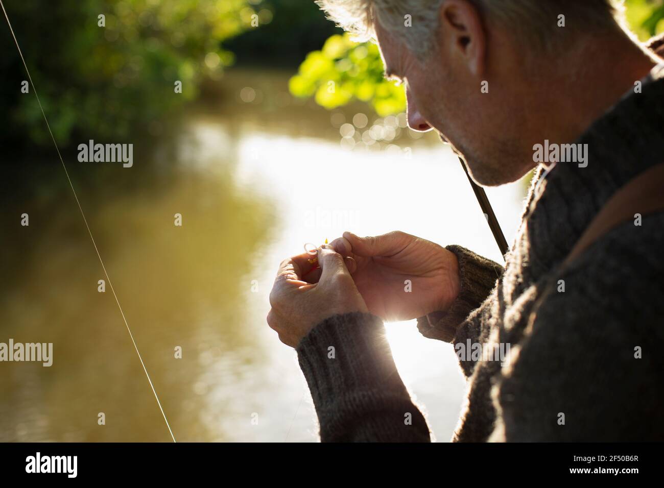 Close up man preparing fly fishing fly at sunny river Stock Photo