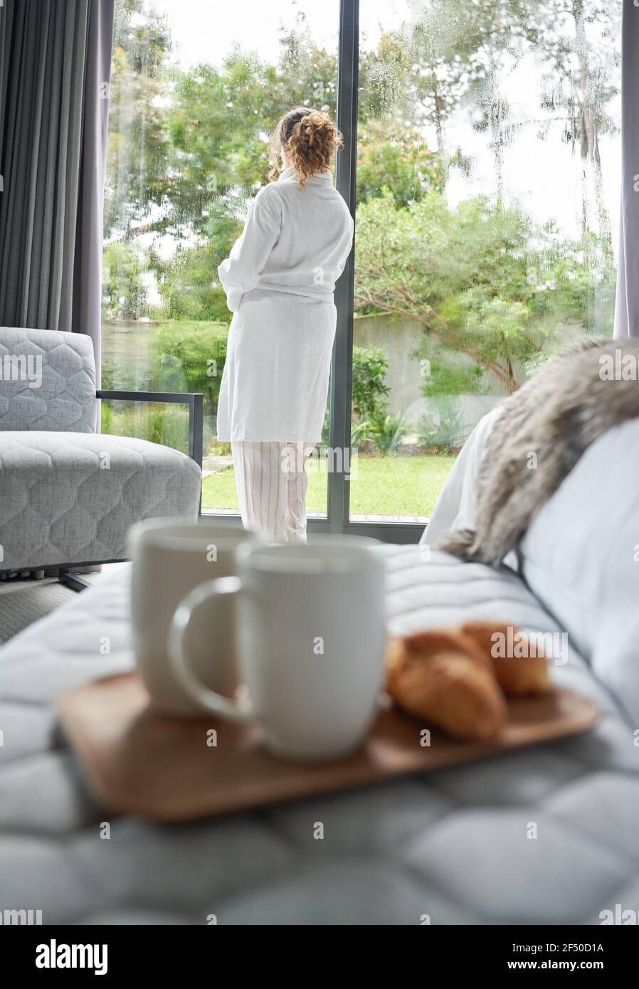 Woman in bathrobe standing at bedroom window Stock Photo