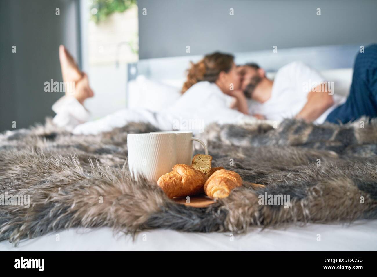 Affectionate couple kissing on bed behind croissant and coffee cup Stock Photo
