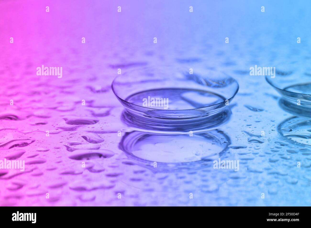 Contact lenses, on pink-blue background. Two contact lenses with water drops on pink-blue background. Stock Photo