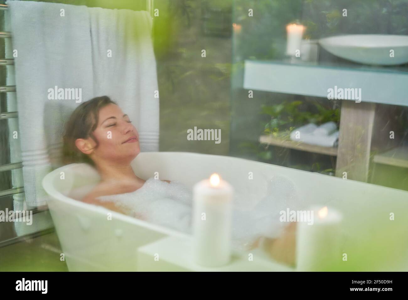 Serene woman enjoying bubble bath with candles in luxury bathroom Stock Photo