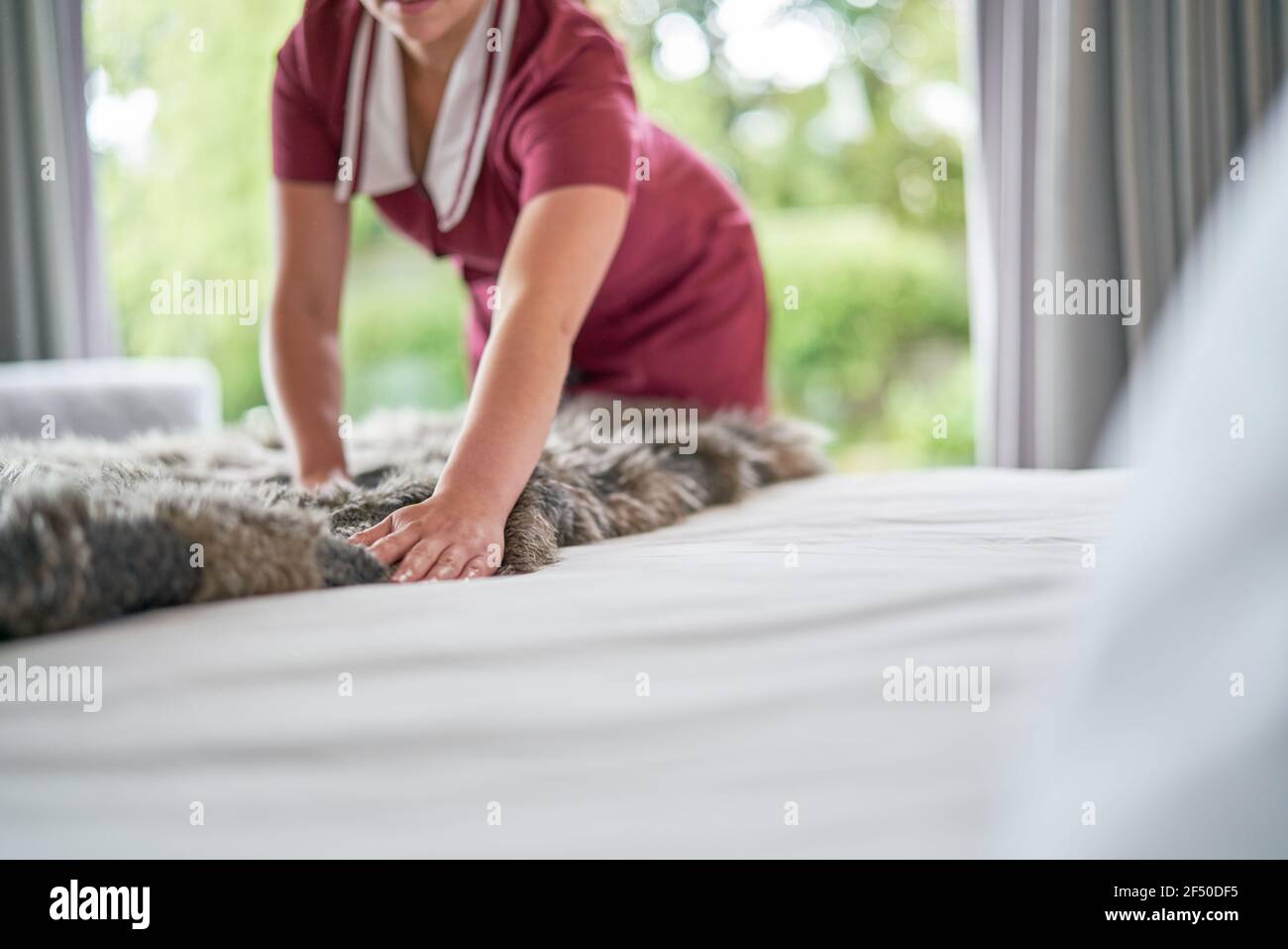 Female hotel maid arranging blanket over made bed in hotel room Stock