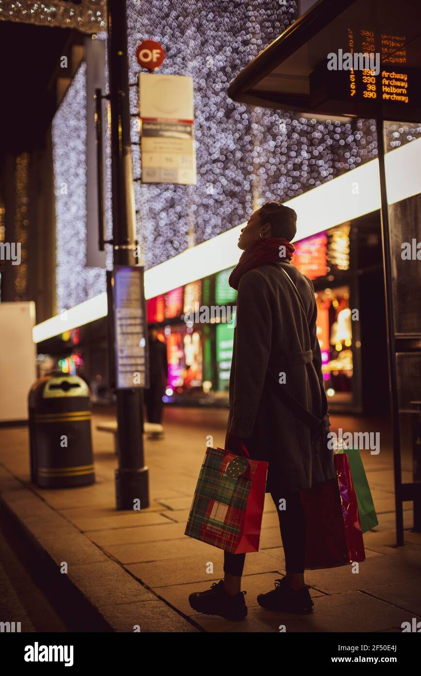 Young woman with Christmas shopping bags on city sidewalk at night Stock Photo