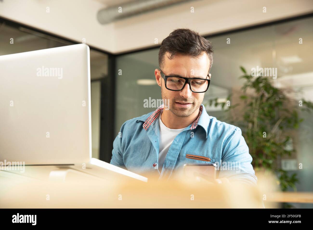 Businessman using smart phone at laptop in office Stock Photo