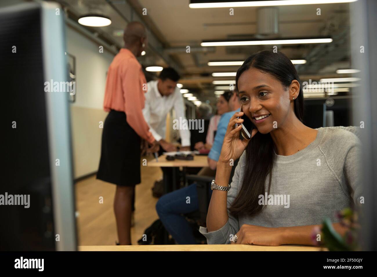 Smiling businesswoman talking on smart phone in open plan office Stock Photo