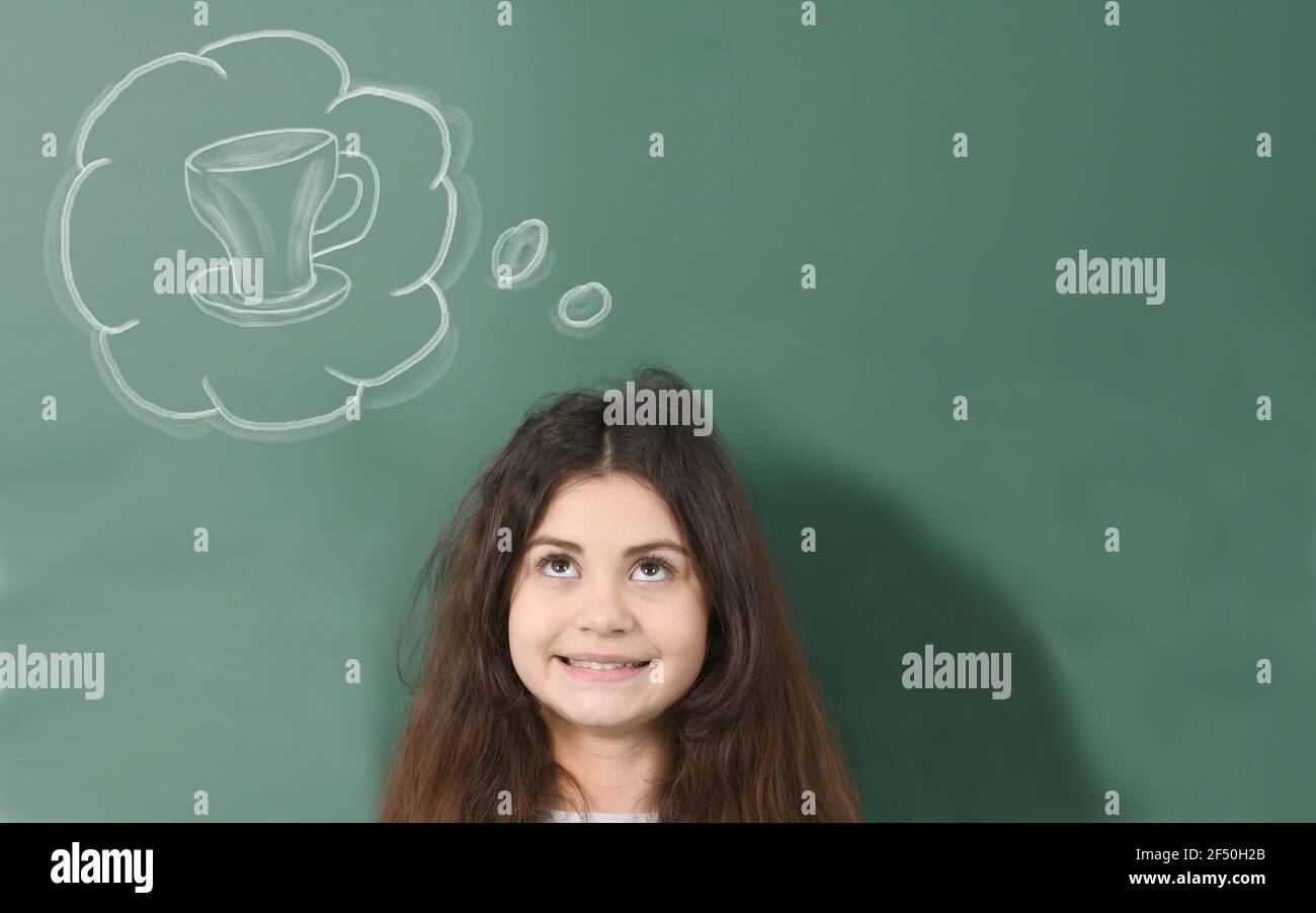 Smiling pre-adolescent child  dreams about cup of tea on green school board background. Stock Photo