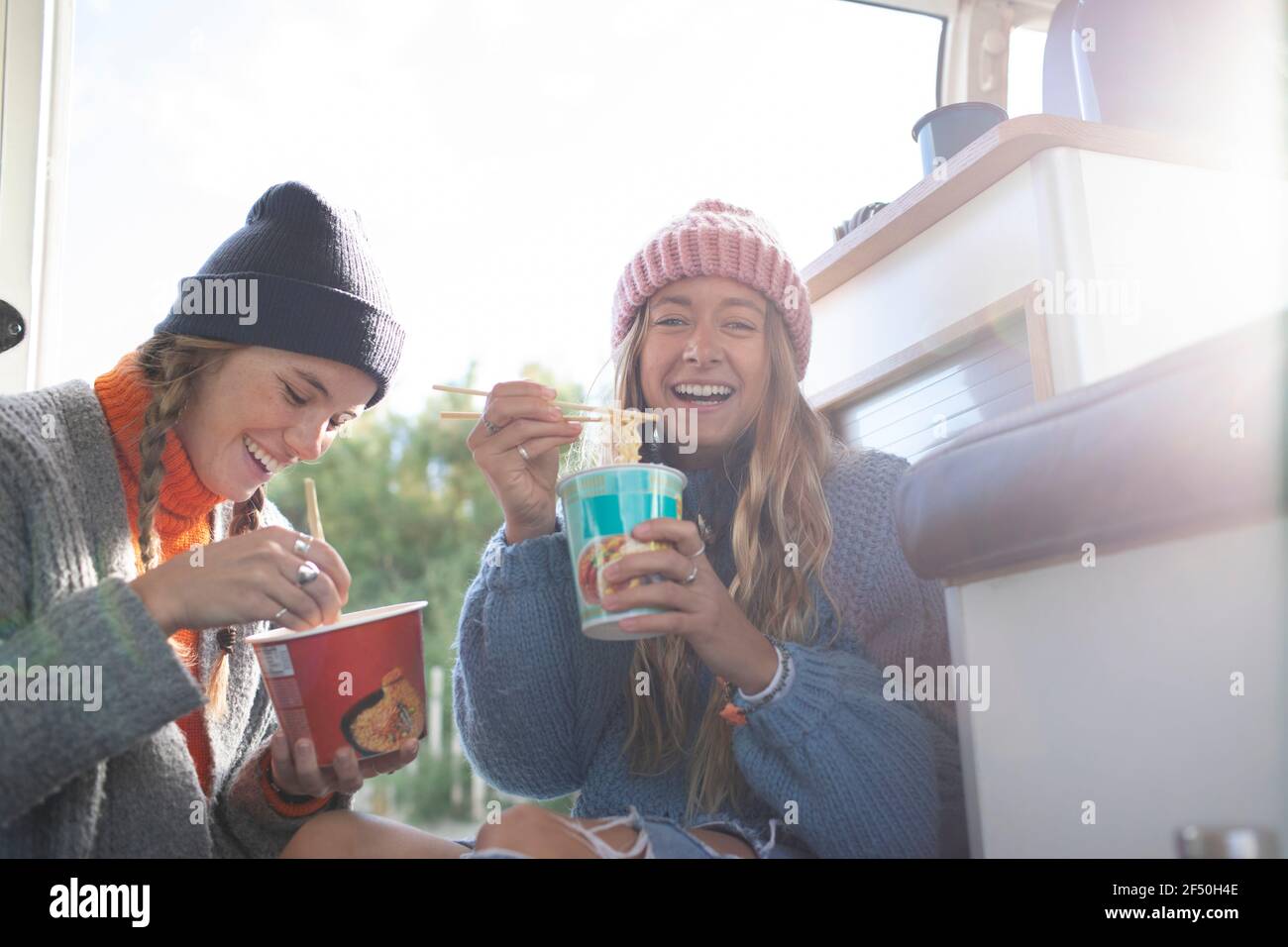 Portrait happy young women eating instant noodles in camper van Stock Photo