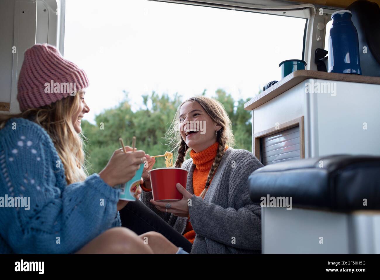 Happy young women friends eating instant noodles in camper van Stock Photo