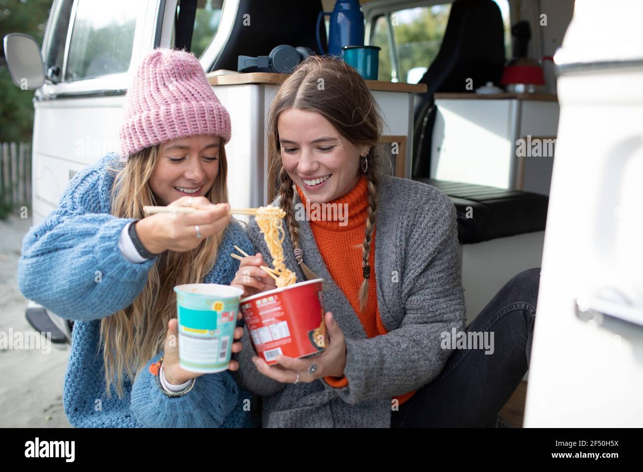 Young women friends sharing instant noodles at camper van doorway Stock Photo