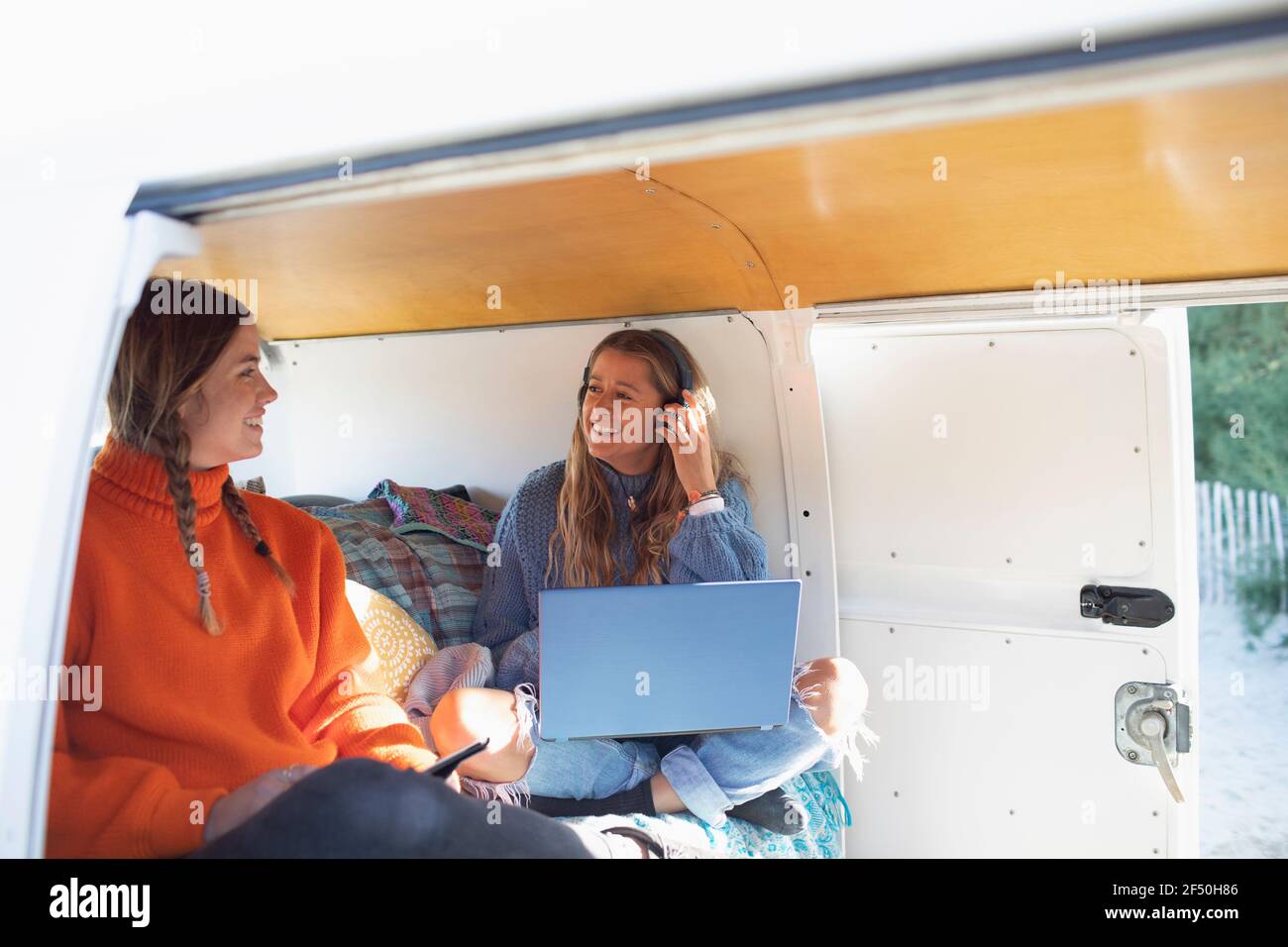 Happy young women friends using laptop and smart phone in camper van Stock Photo