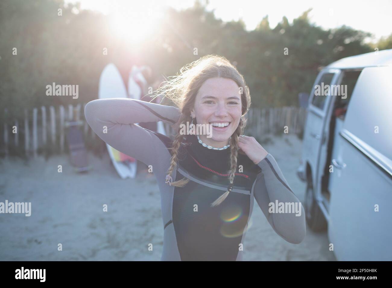 Portrait happy young female surfer in wet suit outside sunny van Stock Photo
