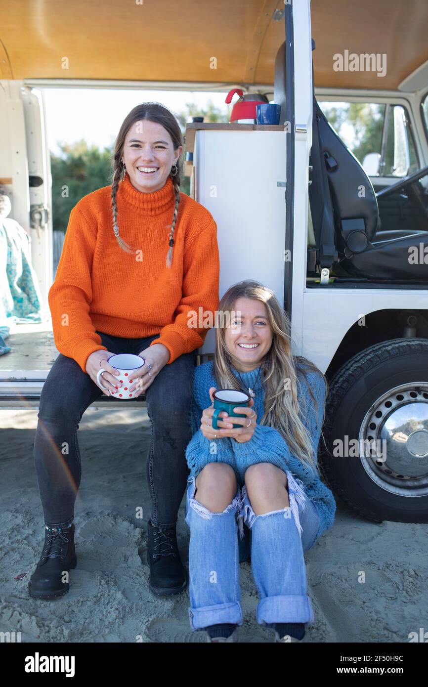 Portrait happy young women friends drinking coffee at camper van Stock Photo