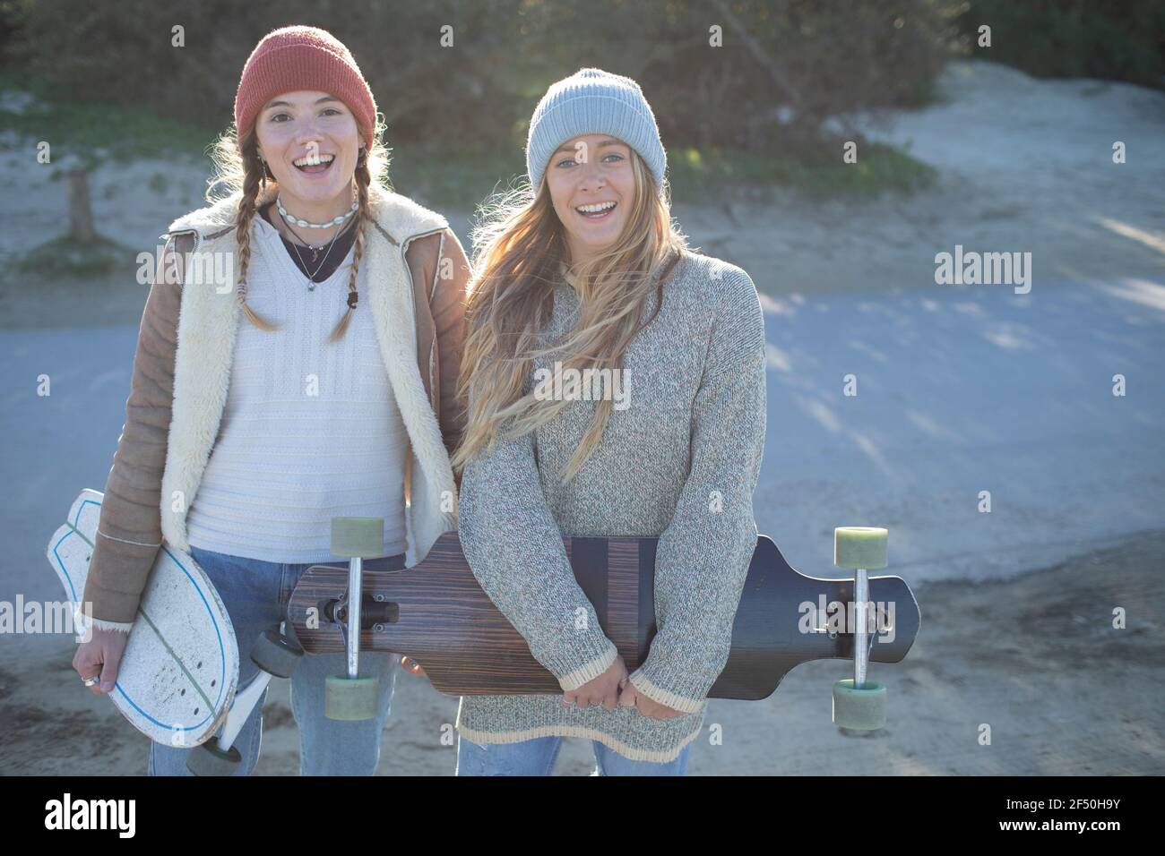 Portrait happy young women friends in knit hats with skateboards Stock Photo